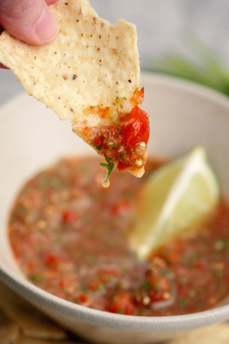 Tortilla chip being dipped into a garden fresh salsa with a wedge of lime in the background